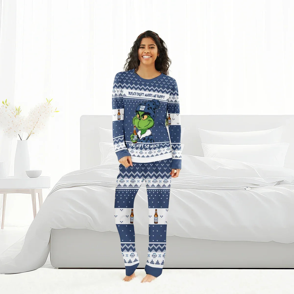 Smiling woman in blue Busch Light Grinch family pajamas standing in bright white bedroom