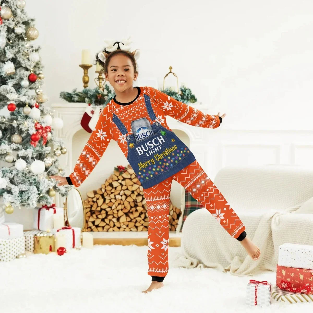 Smiling child in red Christmas pajamas with Busch Light print, reindeer headband, festive living room with tree and gifts