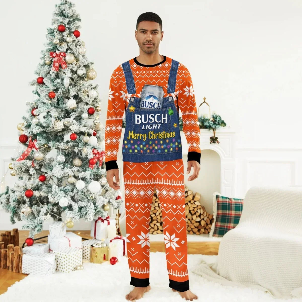 Man wearing orange Christmas pajamas with white snowflakes and denim overalls print featuring Busch Light can and Merry Christmas text, standing by decorated Christmas tree in cozy living room