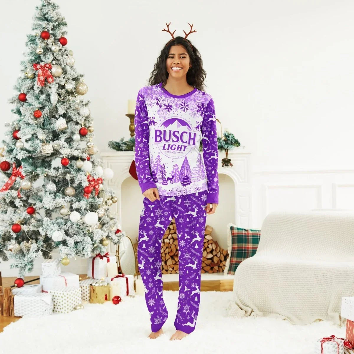 Smiling woman in purple Busch Light winter Christmas pajamas and reindeer antlers by decorated Christmas tree