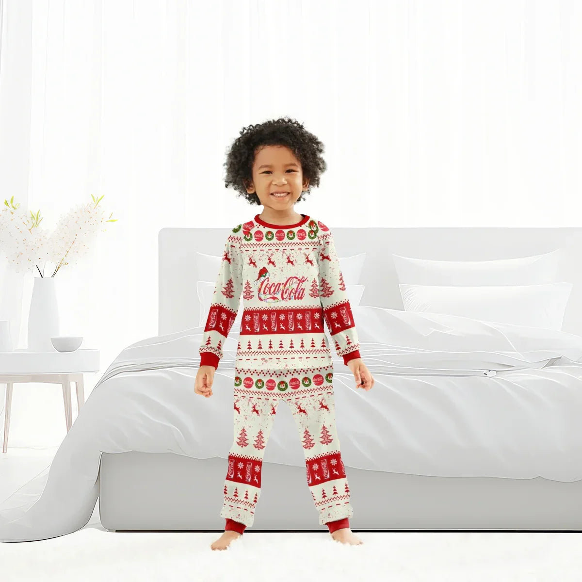 child smiling in Coca-Cola Christmas pajamas with reindeer, trees, and festive patterns in bright bedroom