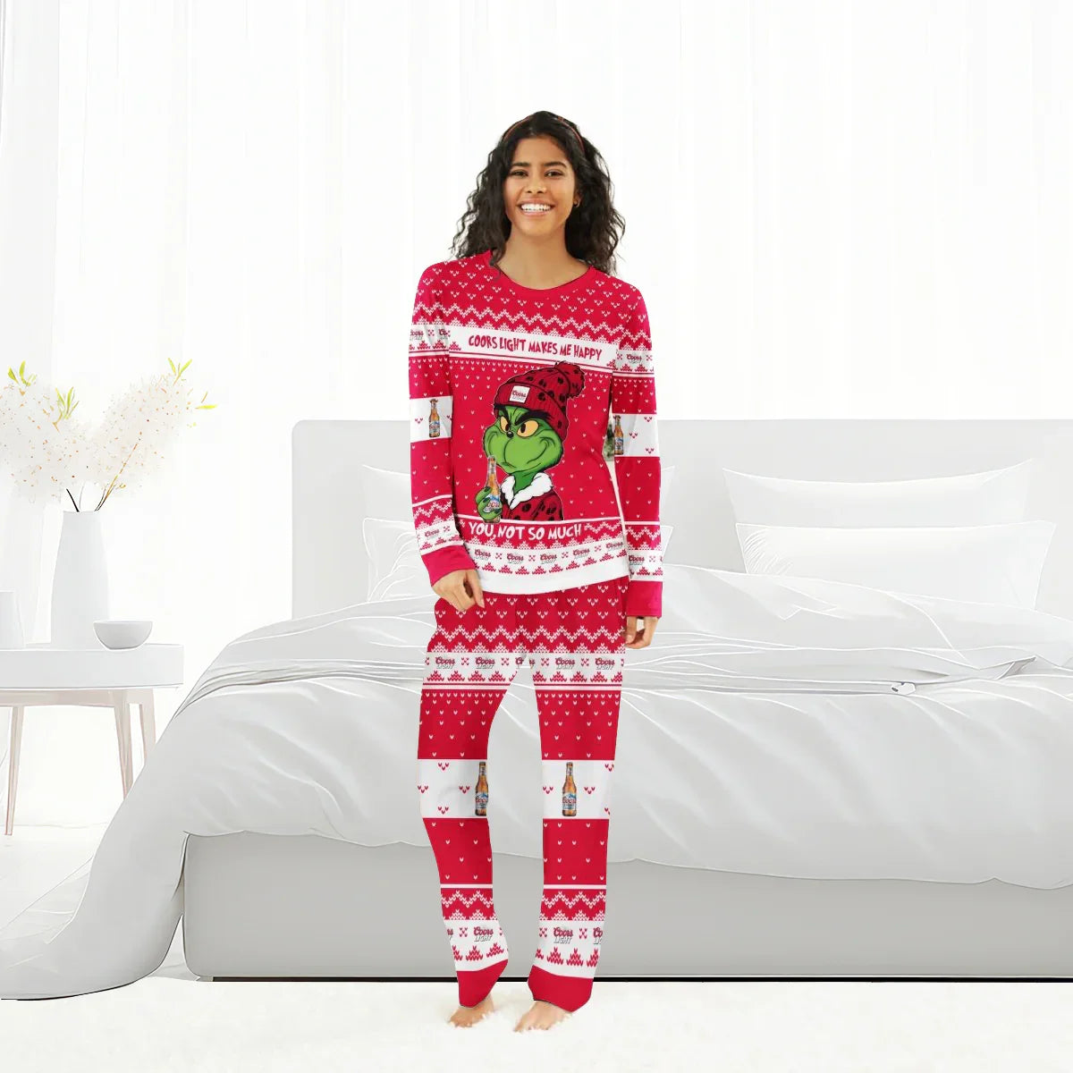 Smiling woman wearing red Coors Light Grinch family Christmas pajamas in bright modern bedroom