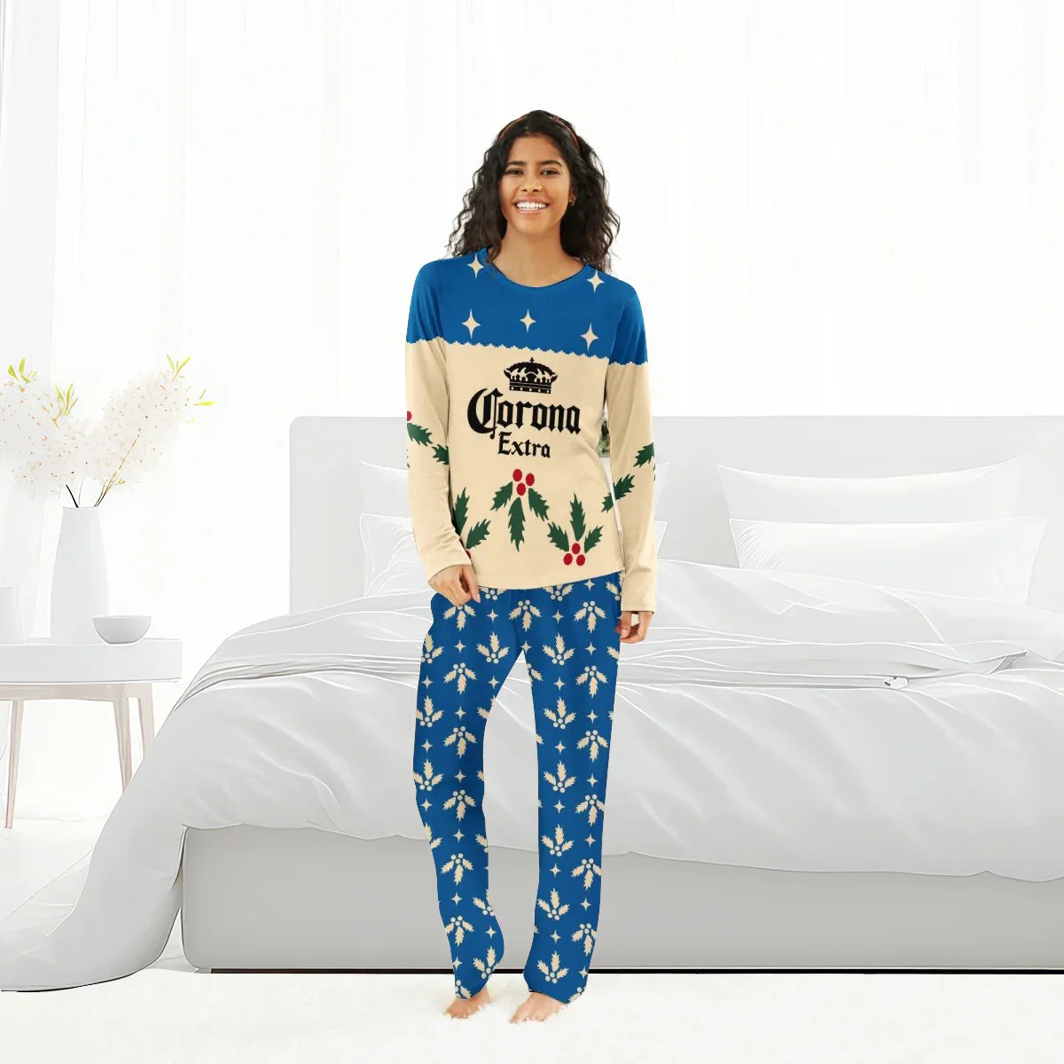Smiling woman wearing blue and cream Corona Extra Christmas pajamas with holly pattern in bright bedroom