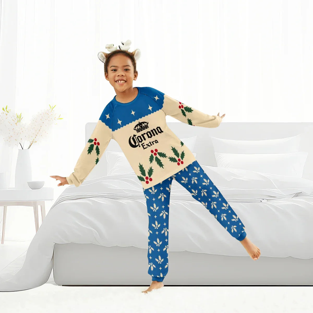 Child wearing Corona Extra Christmas-themed family pajama set with reindeer headband, standing in bedroom