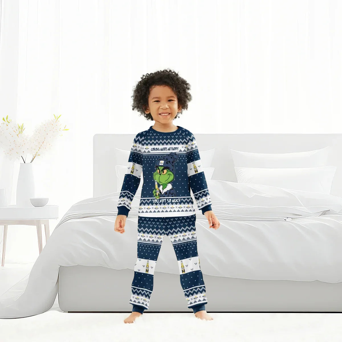 Smiling child in navy blue Grinch-themed Corona Extra family pajamas standing in bright bedroom