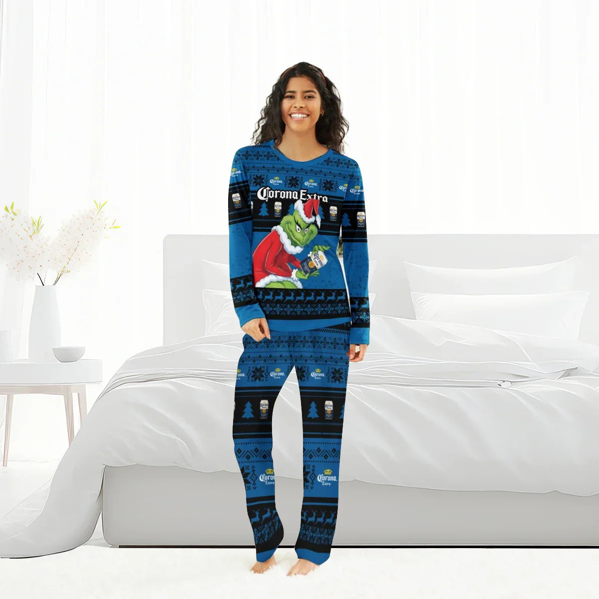Smiling woman in blue Corona Extra Grinch Christmas pajamas standing barefoot in bright bedroom