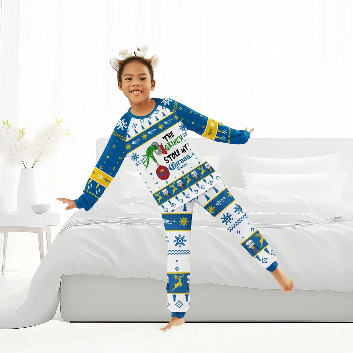 Child wearing Grinch-themed Christmas pajamas with Corona Extra branding in bright bedroom