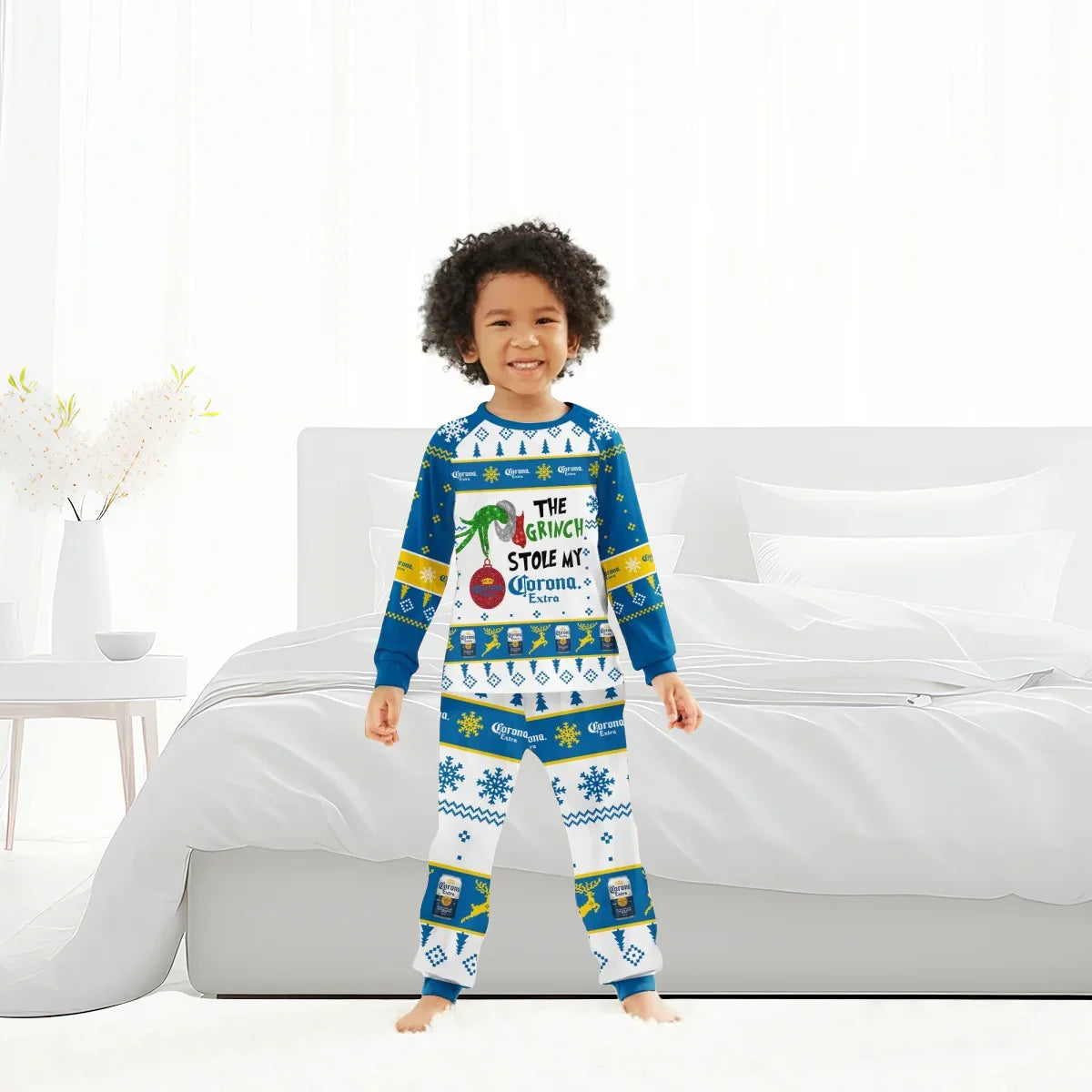 Smiling child in blue and white Grinch-themed Corona Extra holiday pajamas standing in a bright bedroom