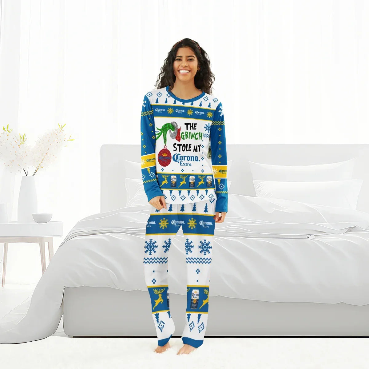 Woman in blue and white Christmas pajamas with Corona Extra and Grinch design standing in a bright bedroom