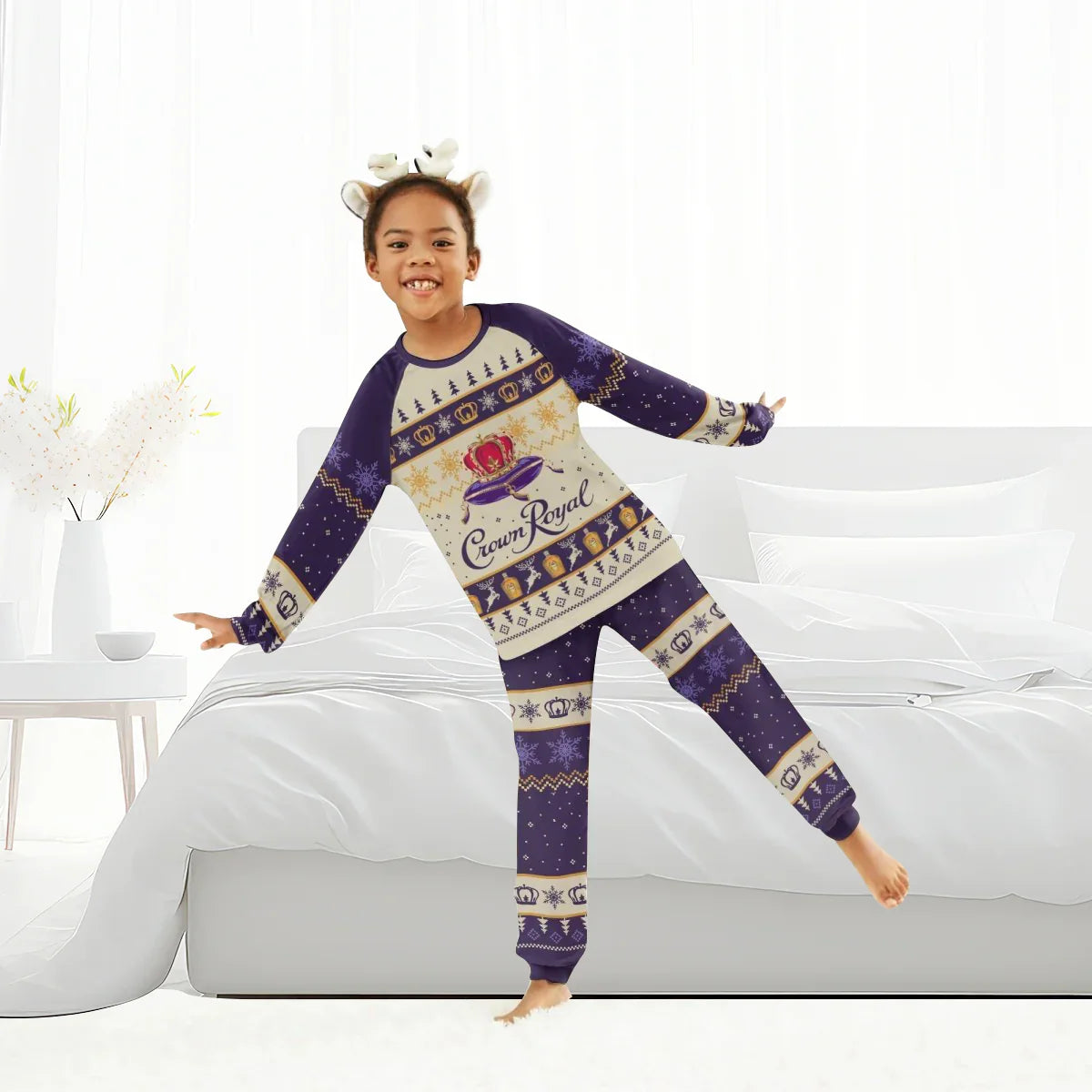 Smiling child wearing Crown Royal Christmas family pajamas and reindeer antler headband in bright bedroom