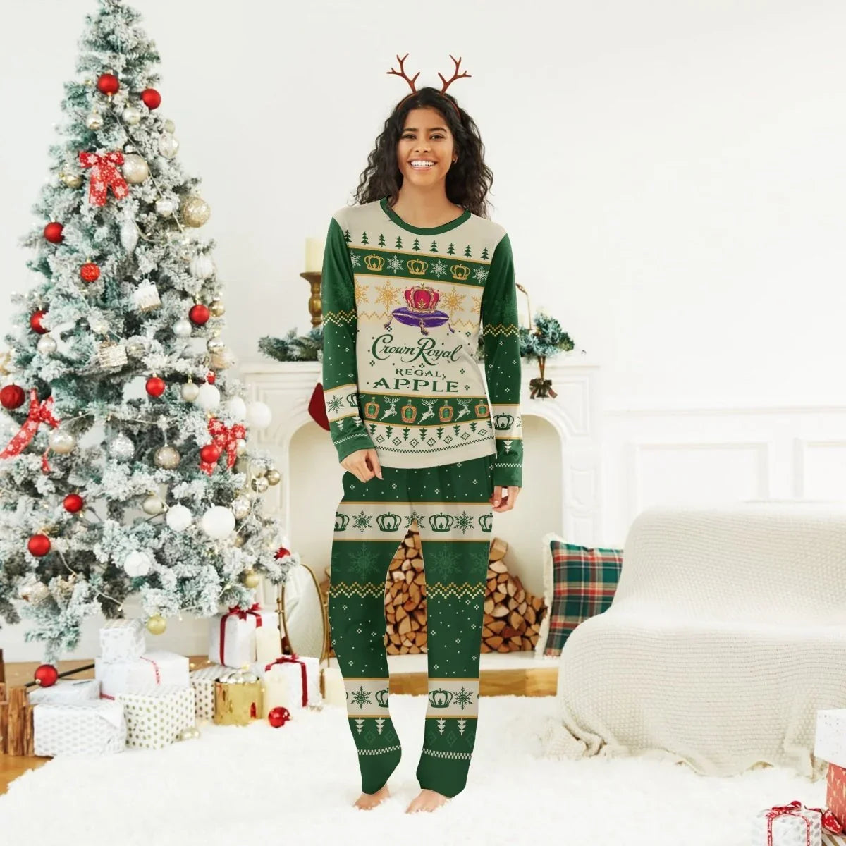 Smiling woman in green Crown Royal Christmas pajamas with antler headband by decorated Christmas tree