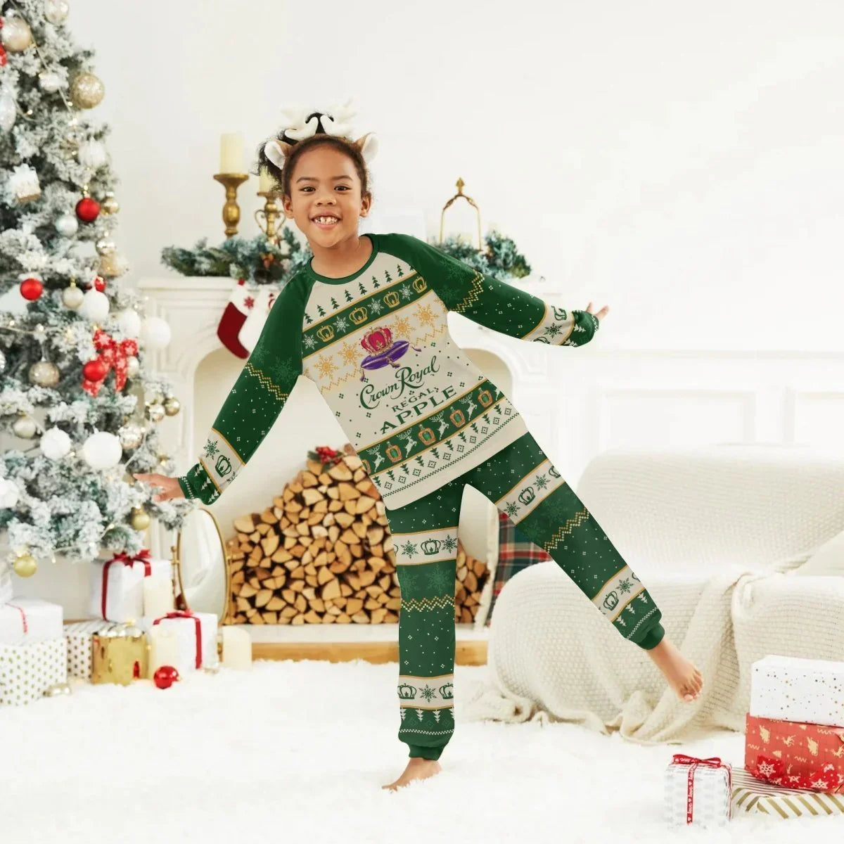 Child in green Crown Royal Apple Christmas pajamas posing in festive living room with decorated tree and presents