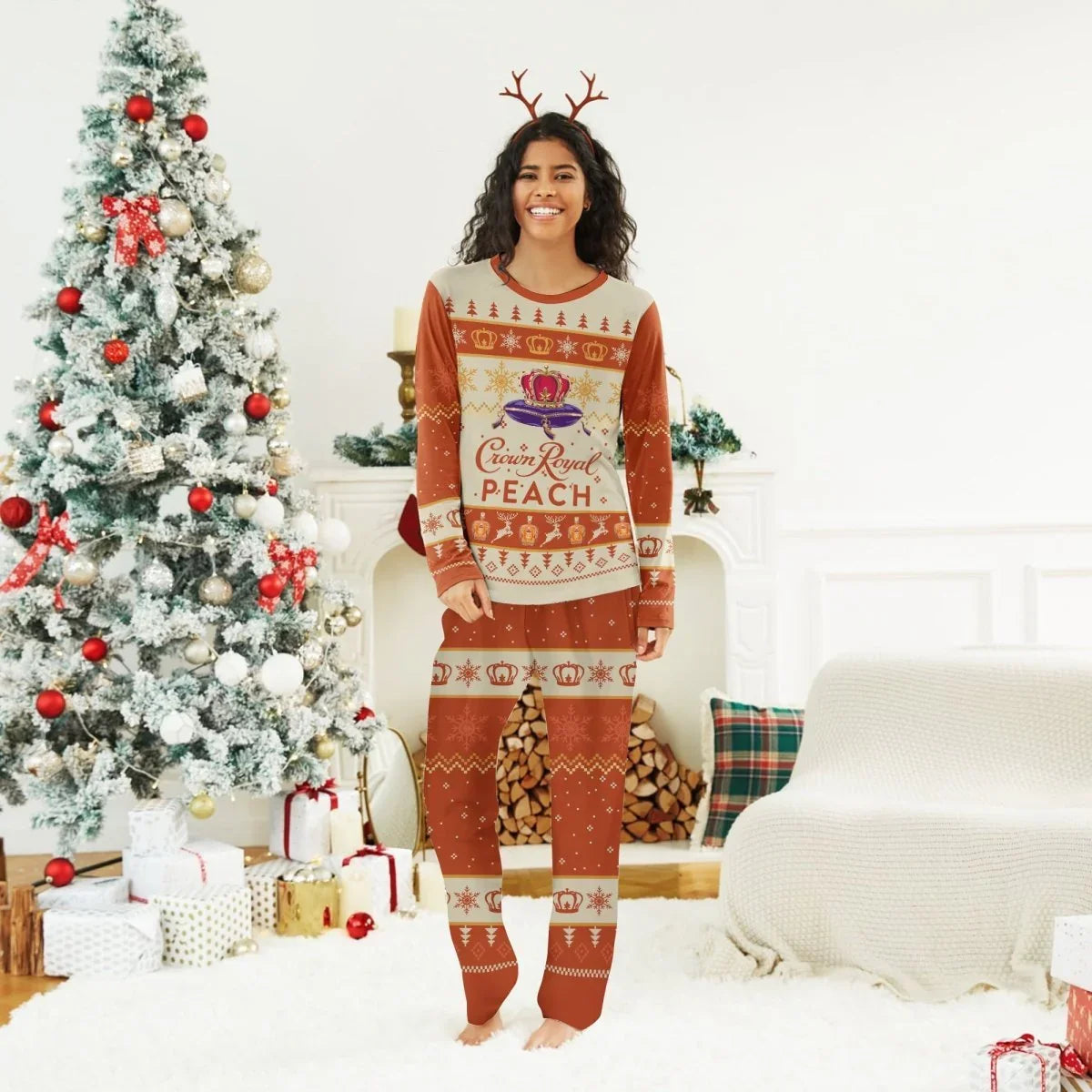 Smiling woman in Crown Royal Peach Christmas pajamas and reindeer antlers by decorated tree and cozy fireplace