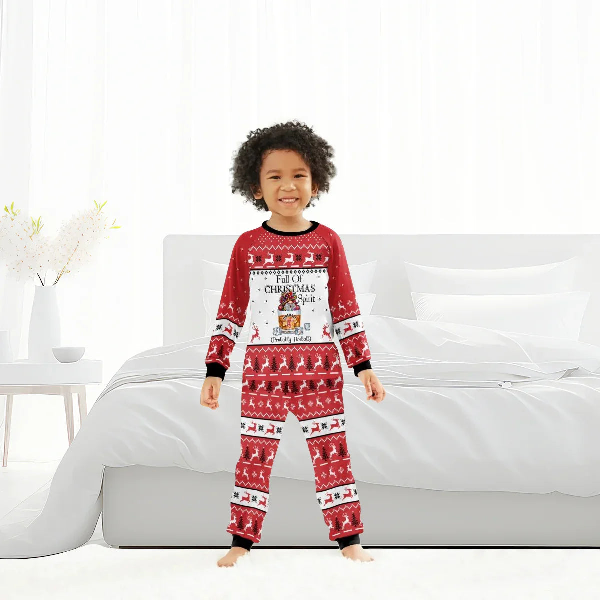 Smiling child in red Christmas pajamas with reindeer and text Full of Christmas Spirit in bright bedroom