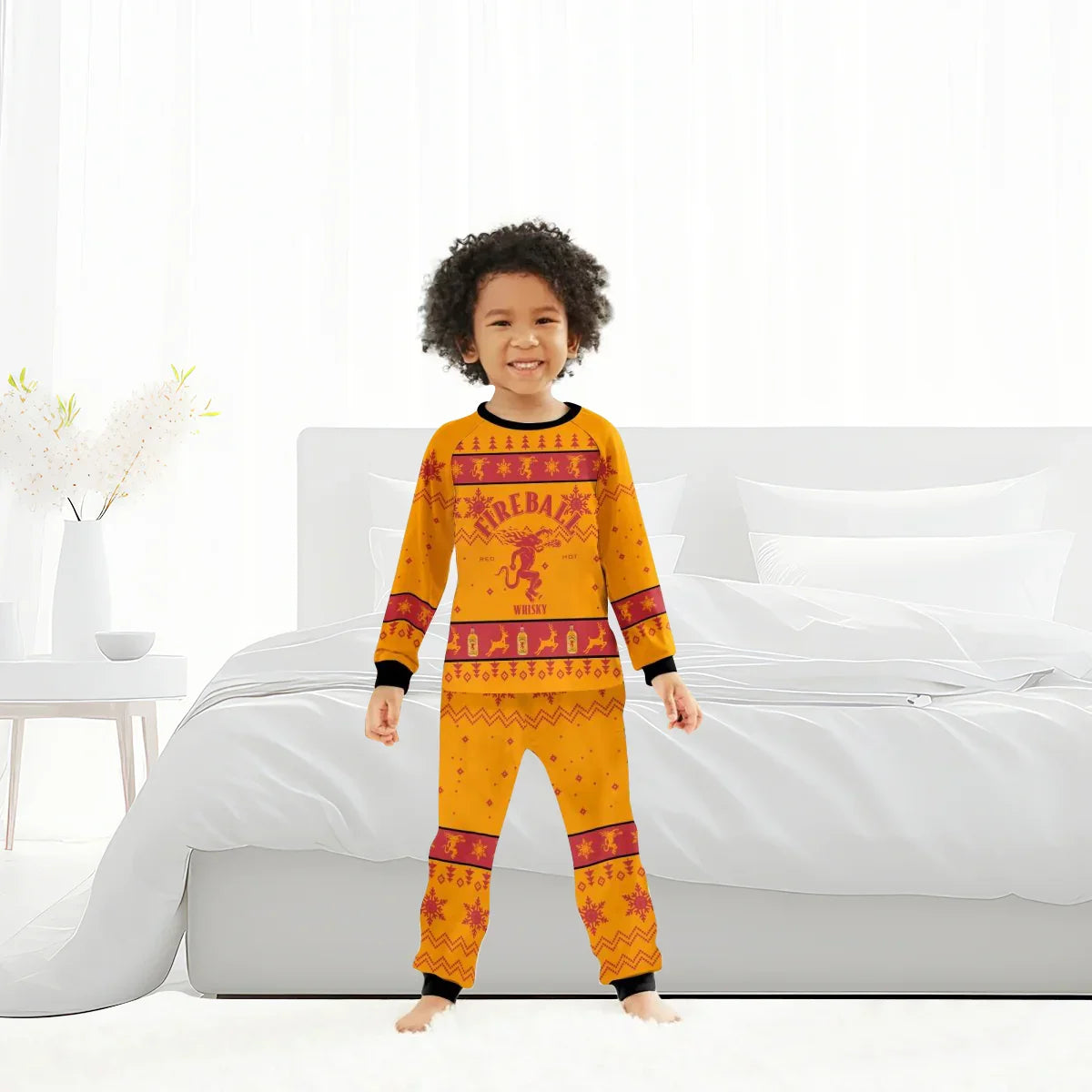 Smiling child wearing orange Fireball Whisky Christmas pajamas standing barefoot in a bright white bedroom