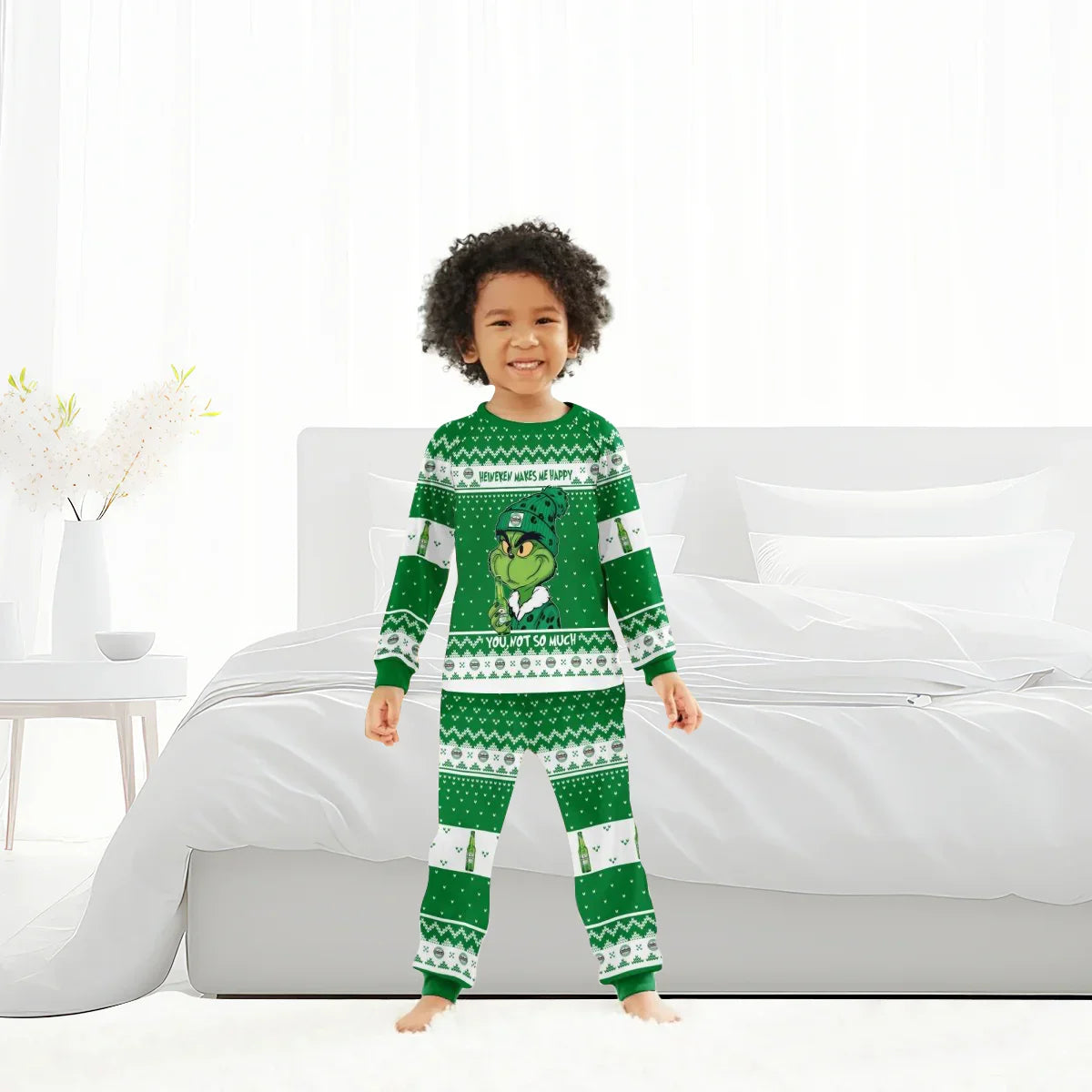Smiling child in green Grinch-themed Christmas pajamas standing barefoot in bright white bedroom