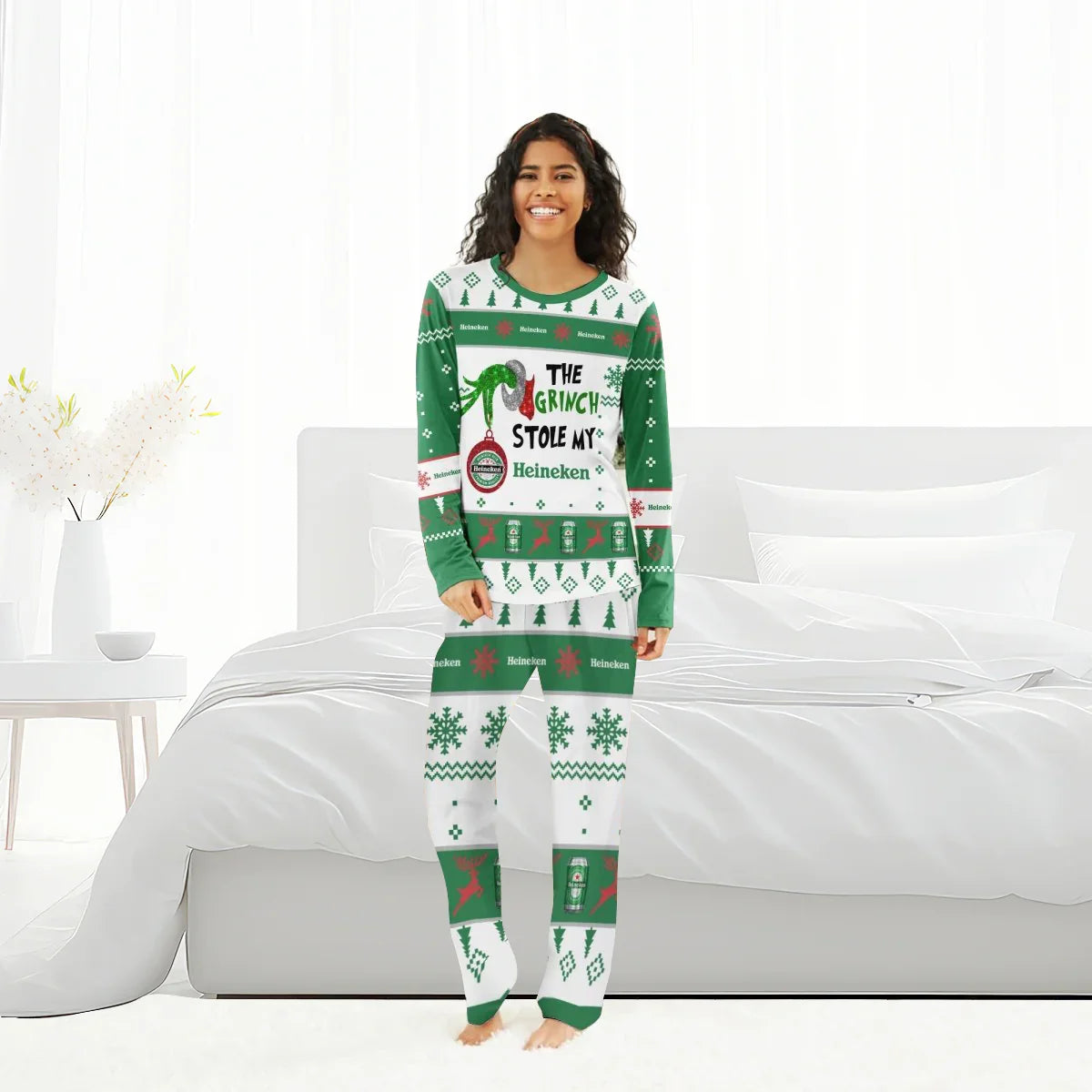 Smiling woman wearing green and white Heineken Grinch Christmas pajamas in bright bedroom
