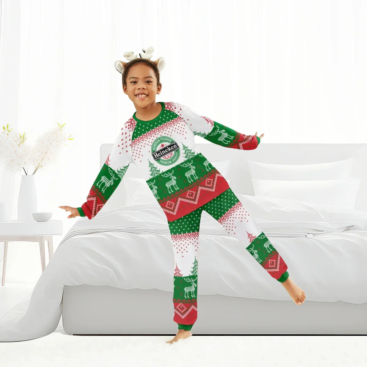 Child wearing Heineken-themed Christmas pajamas with reindeer print and headband in bright bedroom