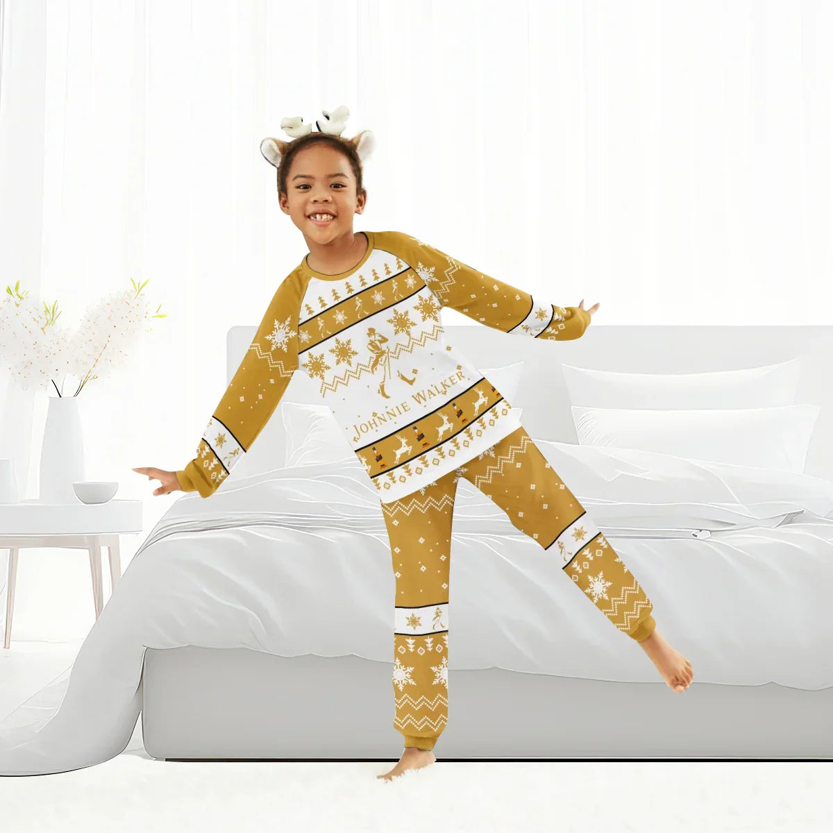 Child in cozy mustard and white Johnnie Walker Christmas family pajama set, standing by white bed
