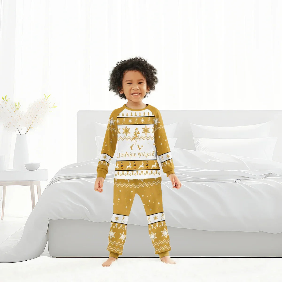Smiling child wearing gold and white Johnnie Walker Christmas pajamas standing barefoot in modern white bedroom
