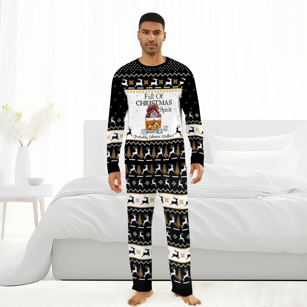 Man wearing black Christmas pajamas with reindeer, trees, and Full of Christmas Spirit Johnnie Walker design, standing barefoot in white bedroom