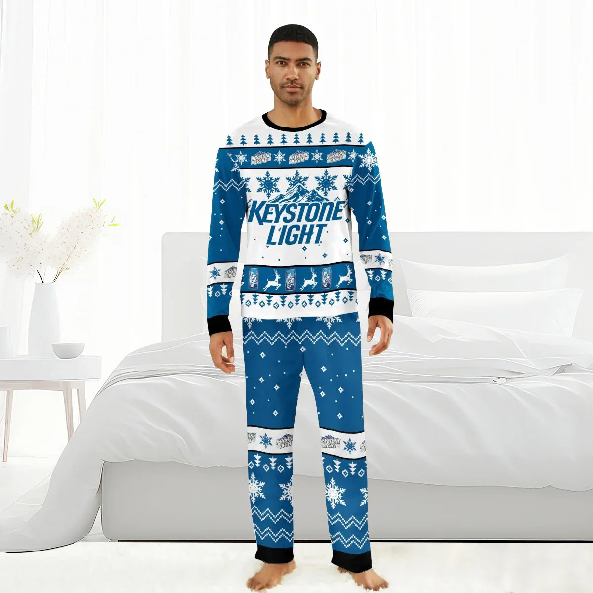 Man wearing blue and white Keystone Light Christmas-themed pajama set with snowflakes and reindeer, standing barefoot in bright bedroom