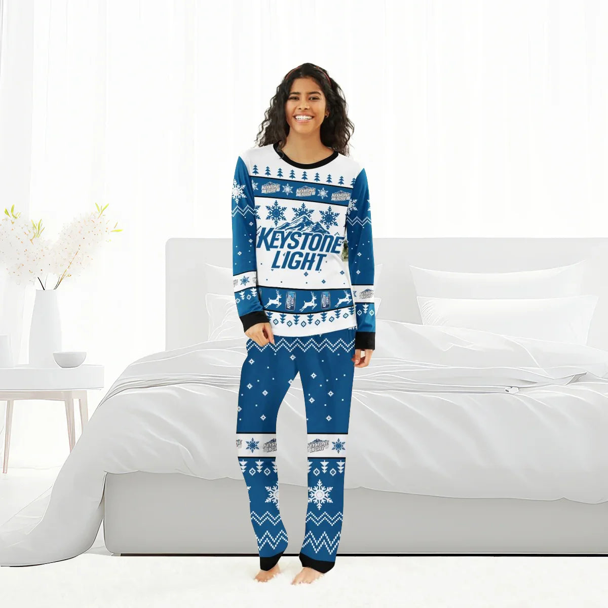 Woman wearing blue and white Keystone Light Christmas-themed pajamas with snowflakes and reindeer in a bright bedroom