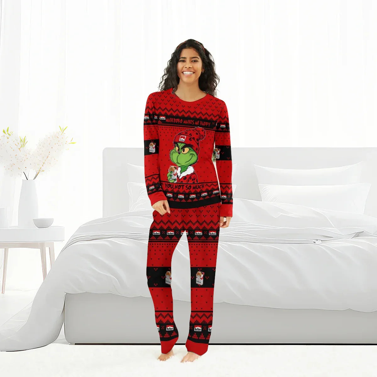 Woman wearing red Marlboro and Grinch-themed Christmas pajamas standing in a bright modern bedroom