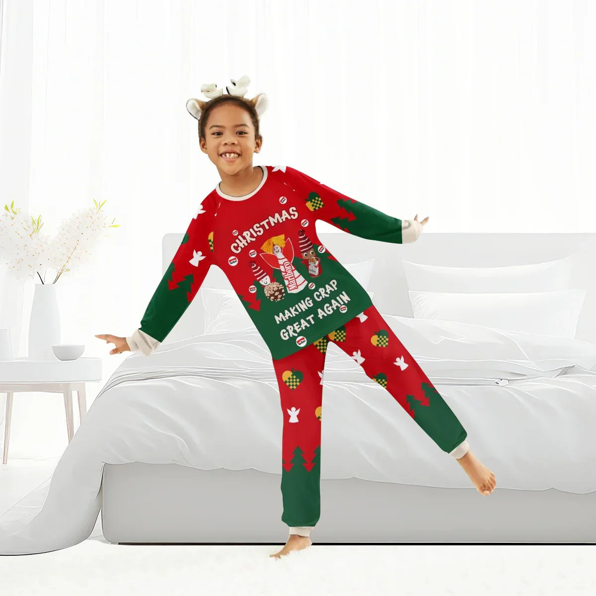 Smiling child in red and green Christmas pajamas with reindeer headband, posing in bright bedroom