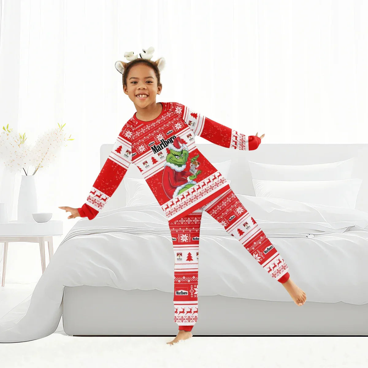 Child wearing red Marlboro Grinch Christmas family pajamas with reindeer headband in bright bedroom