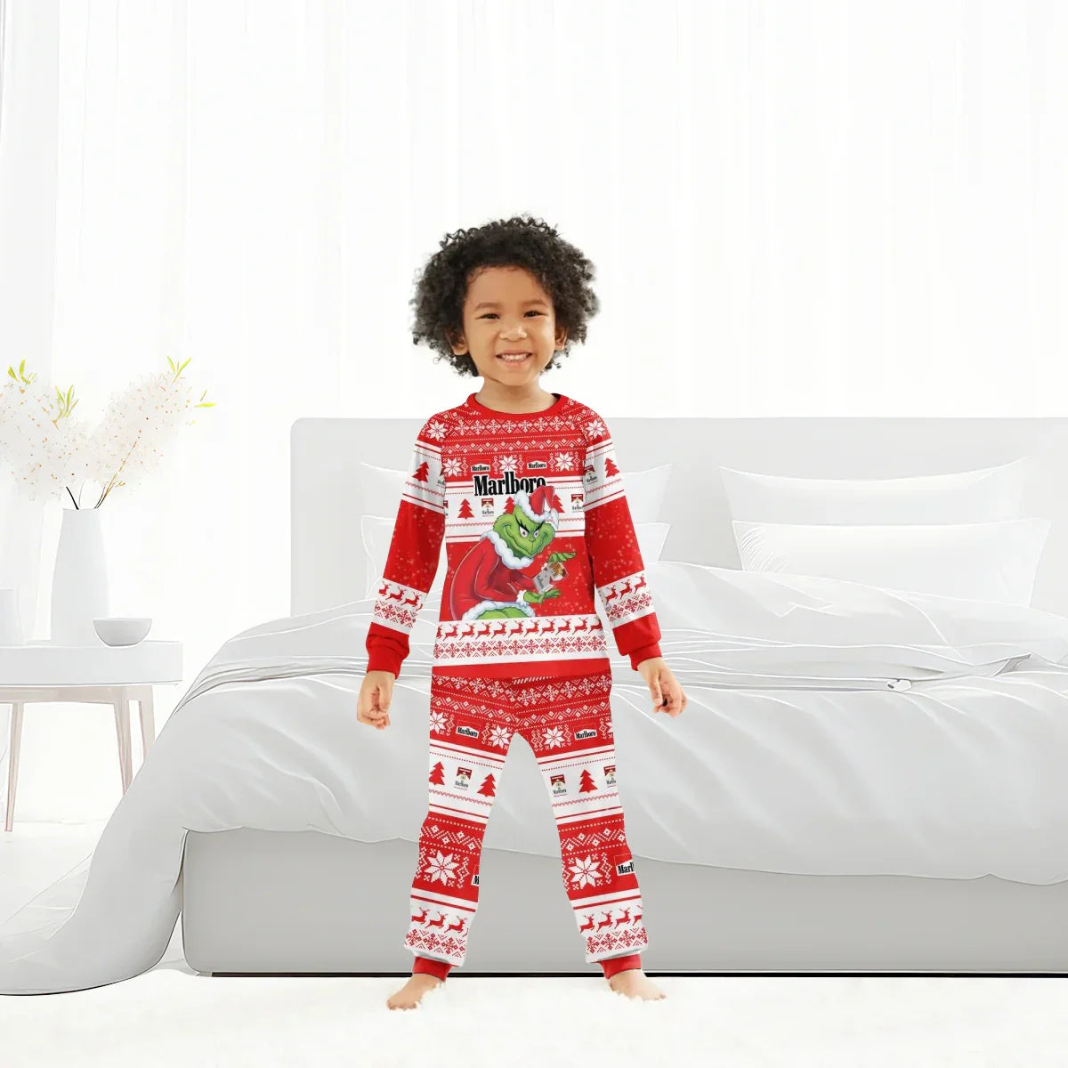 Smiling child in red Marlboro Grinch Christmas family pajamas standing barefoot by white bed