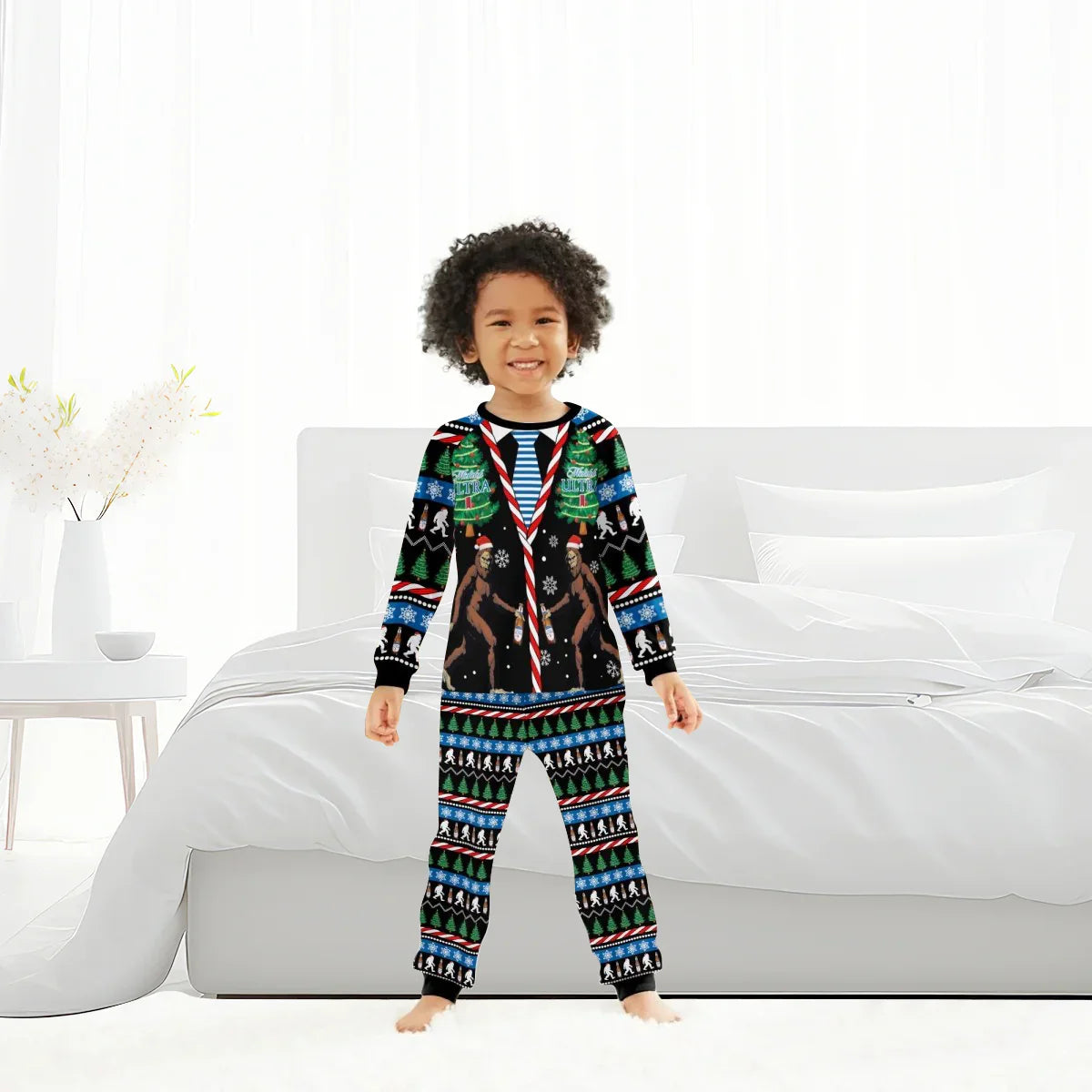 Smiling child wearing black Christmas pajamas with Bigfoot, trees, and holiday patterns in white bedroom