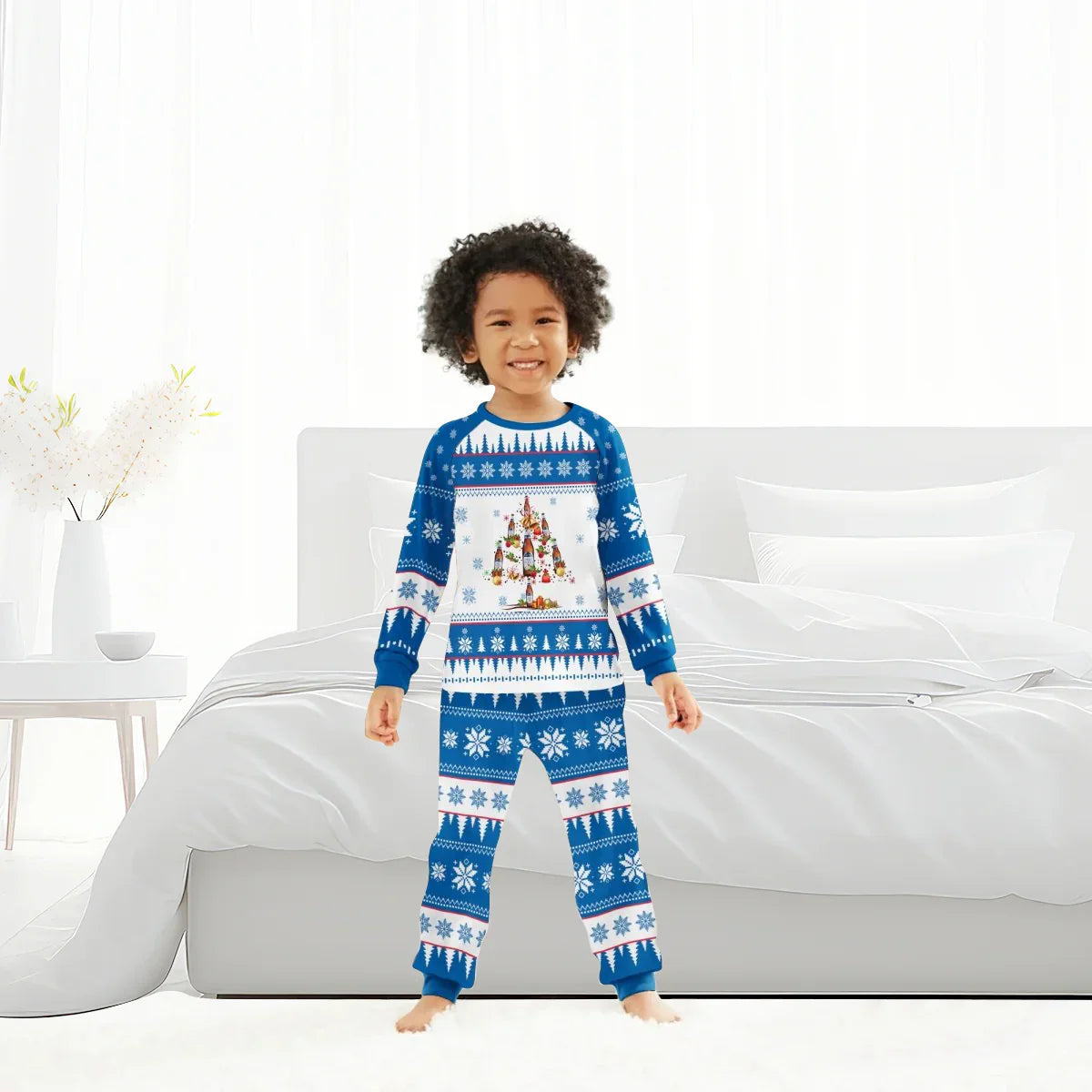 Smiling child in blue and white Christmas tree pajama set with snowflake pattern in bright bedroom