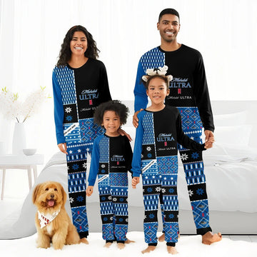 Smiling family of four wearing matching blue Michelob Ultra holiday pajamas with patterns, standing barefoot in bedroom with dog