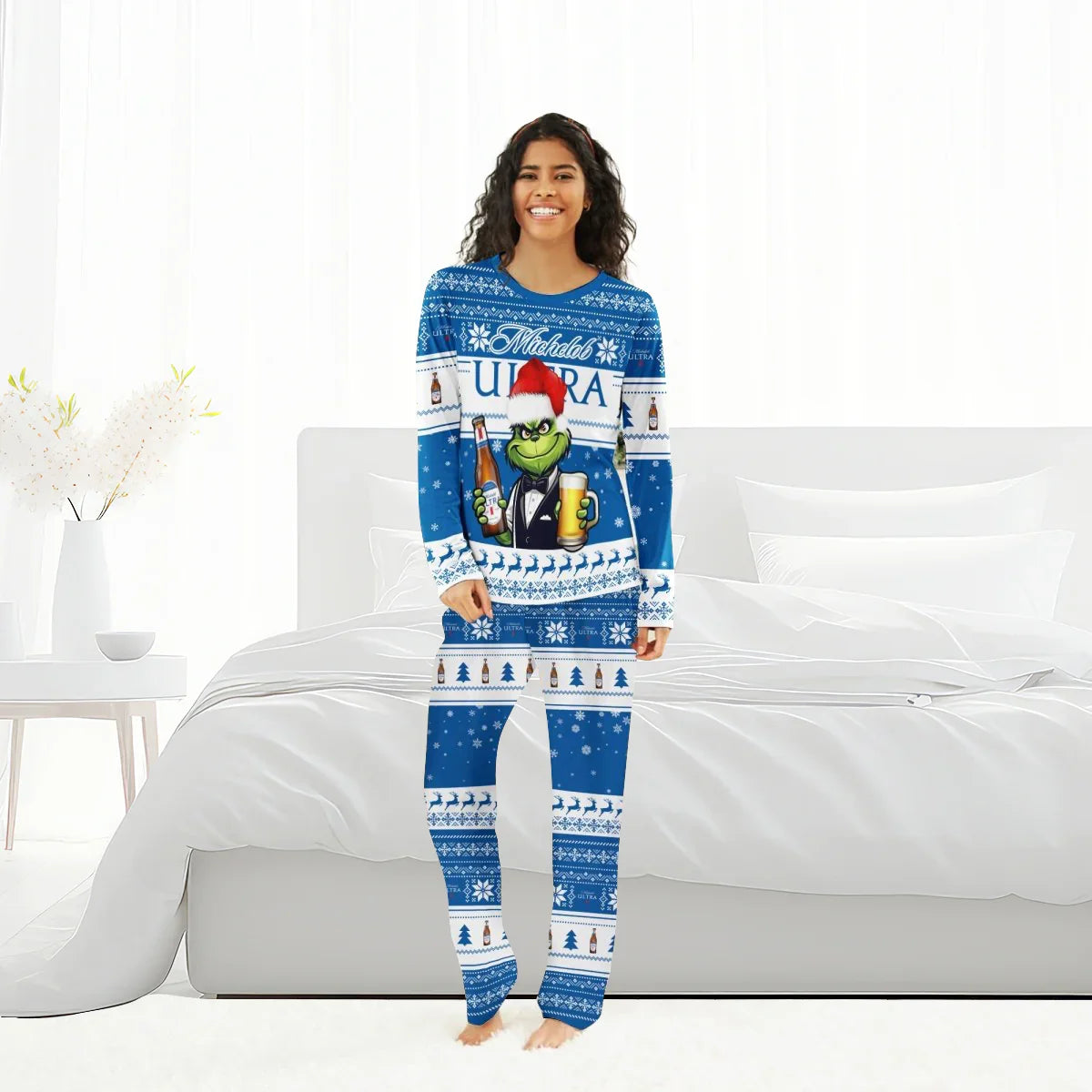 Smiling woman in blue Michelob Ultra Christmas pajamas with Grinch holding beer, standing in white bedroom