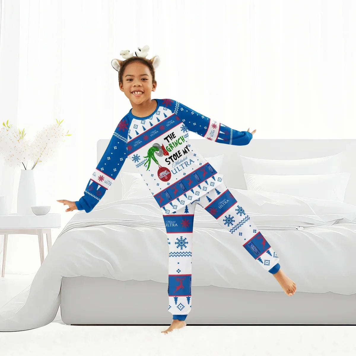 Child in blue and white Grinch-themed Christmas pajamas with reindeer headband in bright bedroom