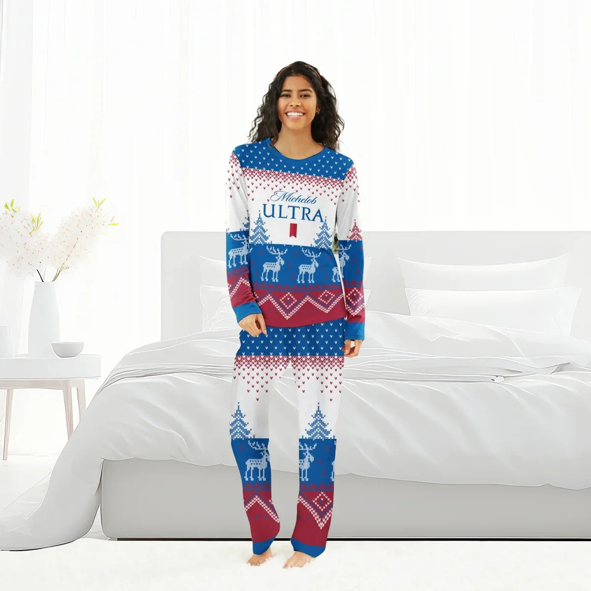 Smiling woman in blue, red, white Michelob Ultra reindeer family pajamas standing barefoot in modern white bedroom