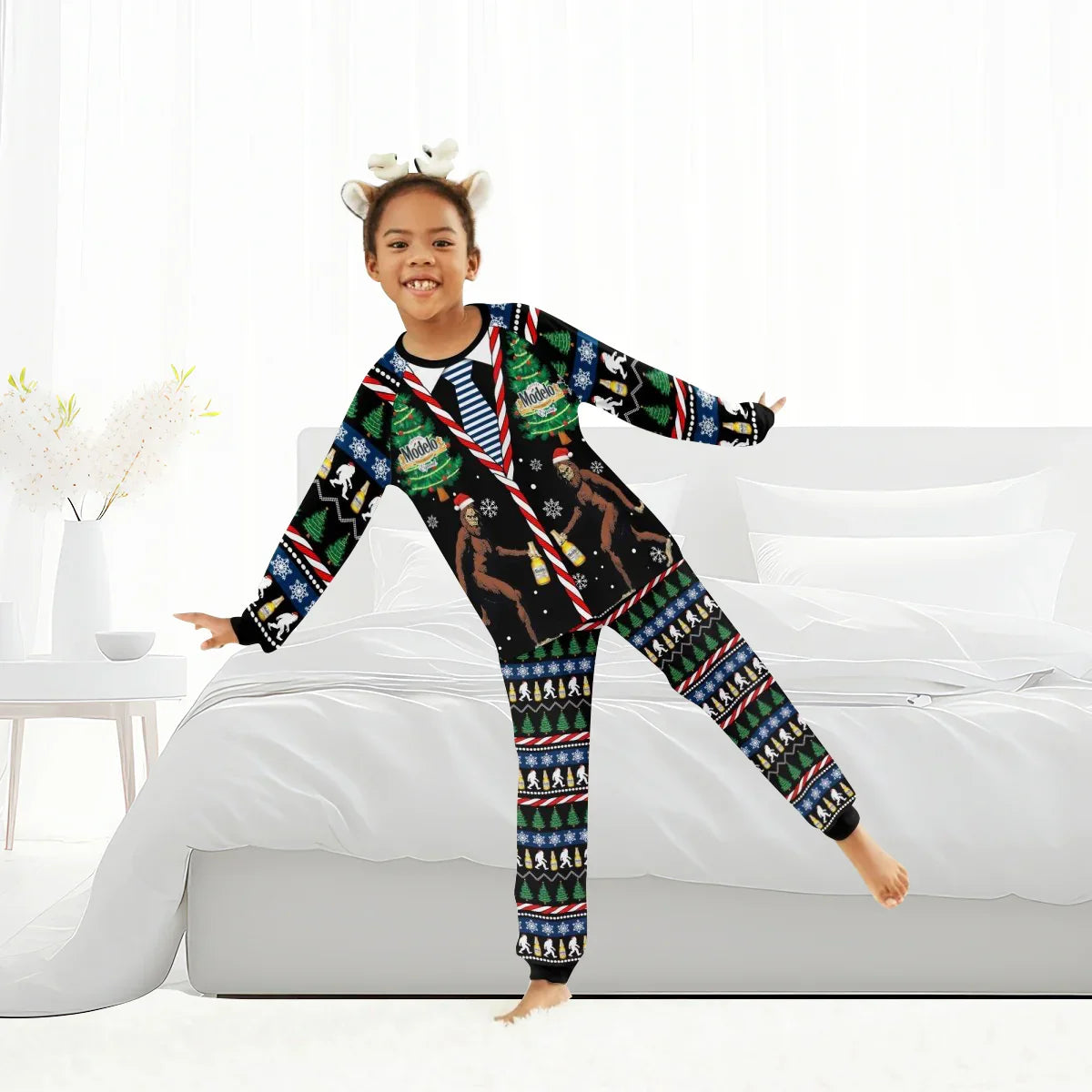 Child wearing colorful Modelo Christmas Bigfoot family pajamas with antler headband in bright bedroom