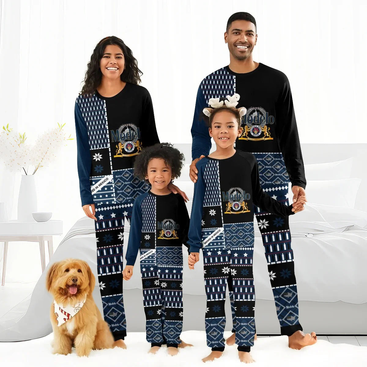 Smiling family in matching black and navy Modelo logo pajamas with winter patterns, standing in bright bedroom with dog