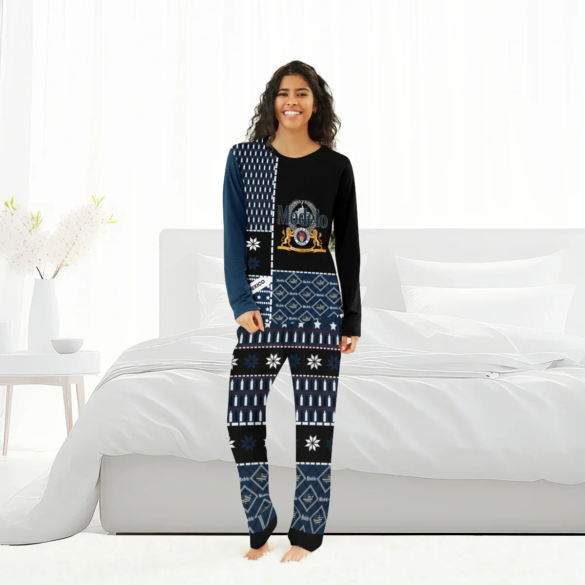Smiling woman wearing black and navy Modelo branded family pajamas standing barefoot in a bright white bedroom