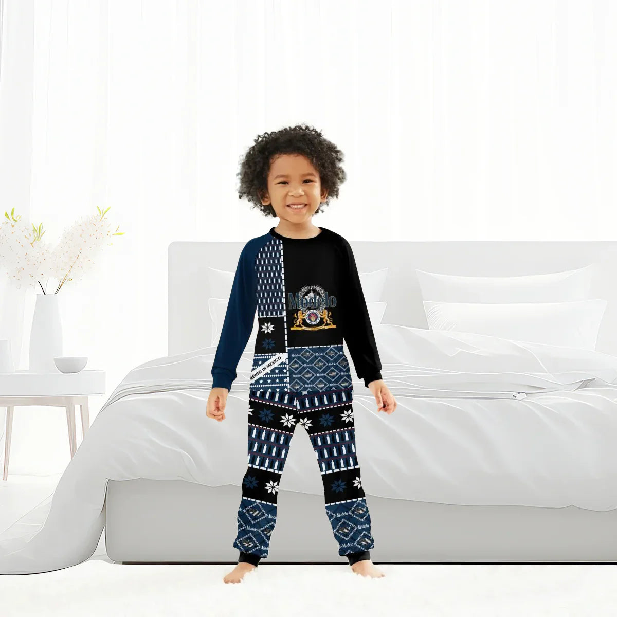 Smiling child wearing black and blue Modelo family pajamas standing barefoot in a bright modern bedroom