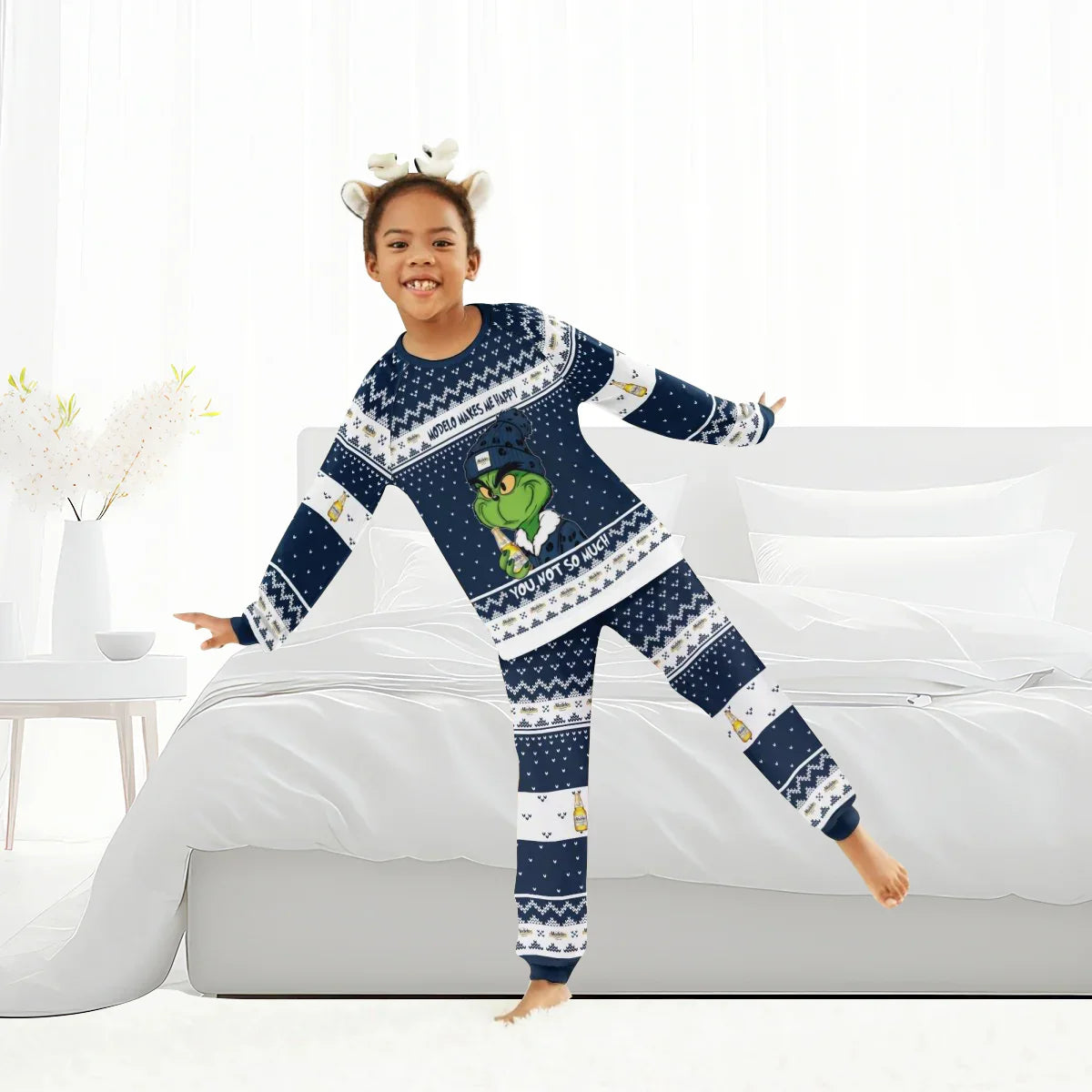 Child wearing navy blue Grinch holiday pajamas with Modelo beer design and reindeer antler headband in bright bedroom