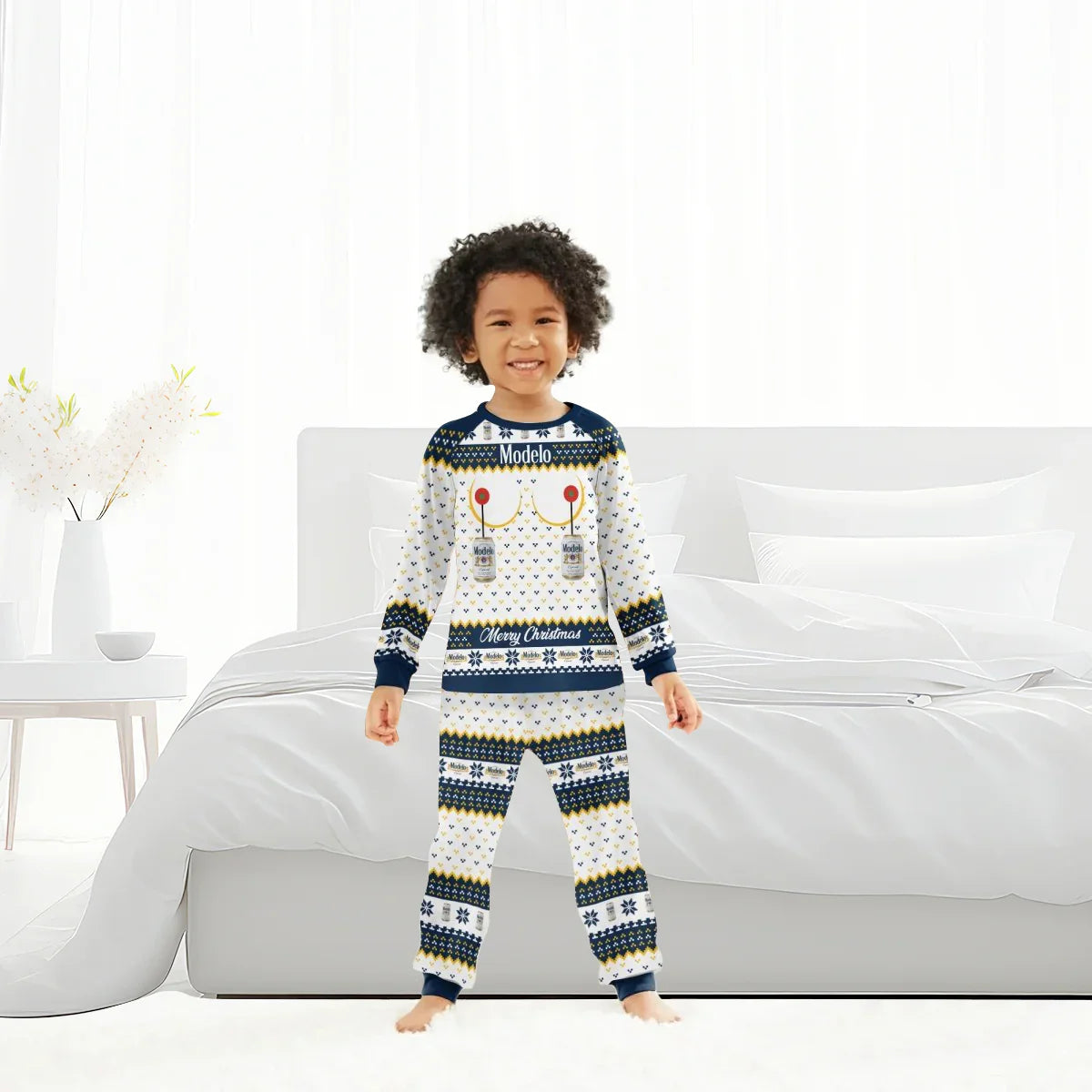 Smiling child in Modelo Merry Christmas family pajamas standing in bright bedroom with white bed