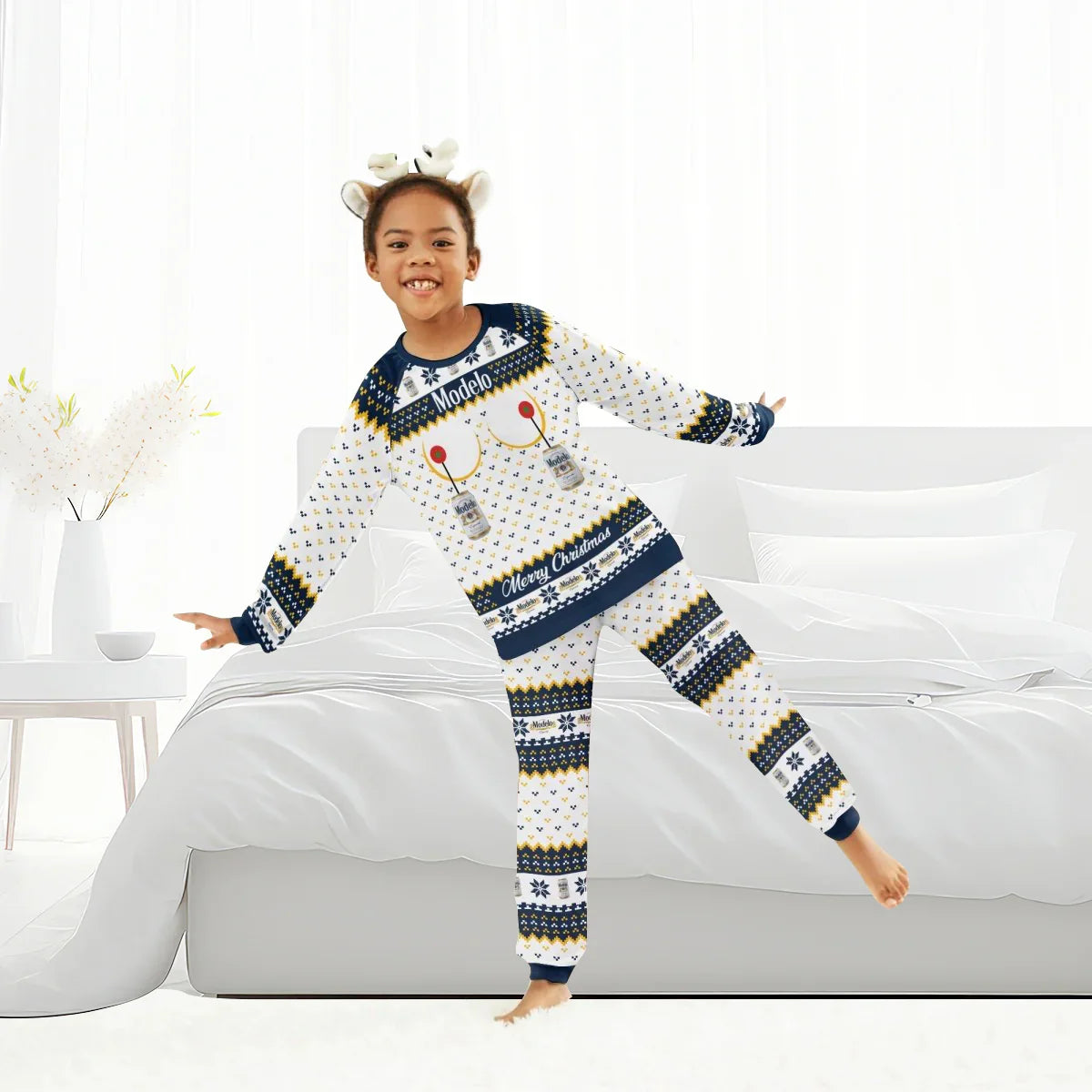 Child in white and navy Modelo Christmas pajamas with reindeer headband in bright bedroom