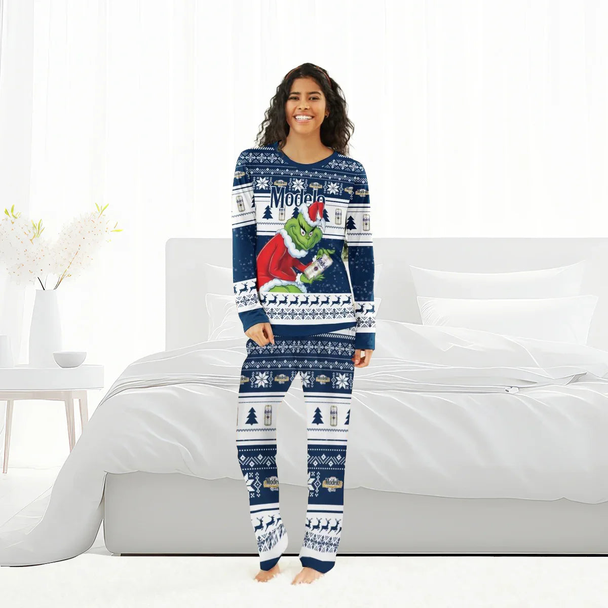 Smiling woman wearing blue Modelo Santa Grinch Christmas pajamas standing in bright bedroom