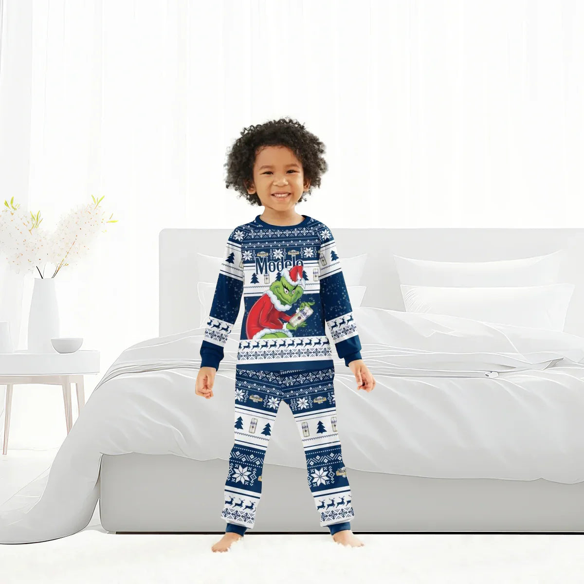 Smiling child in blue Christmas pajamas with Grinch and Modelo beer design, standing in white bedroom
