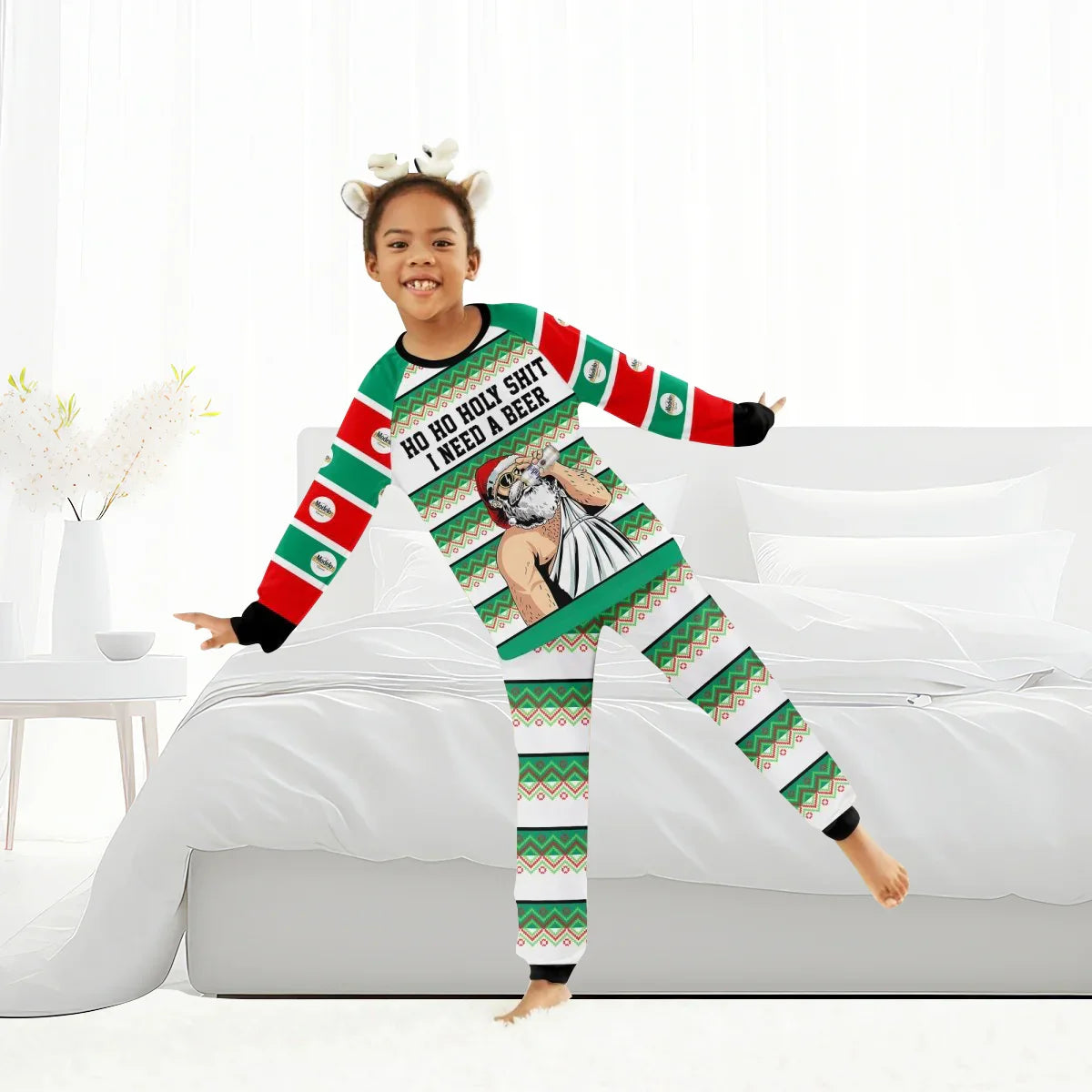 Smiling child wearing colorful Christmas pajamas with Santa and beer text, posing in white bedroom