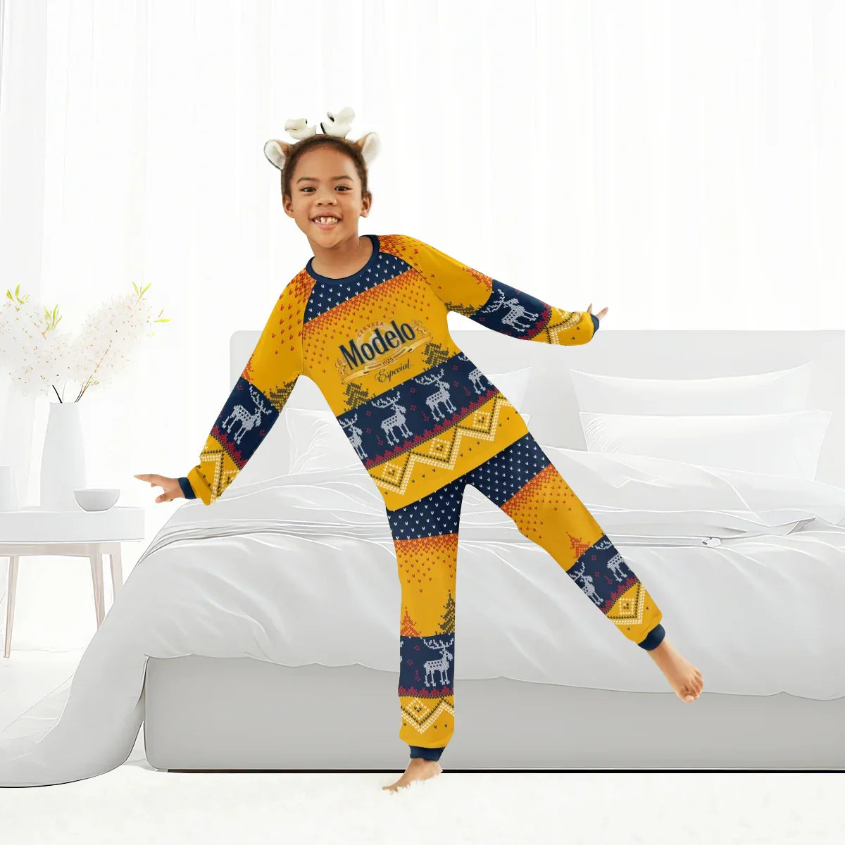 Child wearing Modelo winter reindeer family pajamas and festive antler headband in bright bedroom