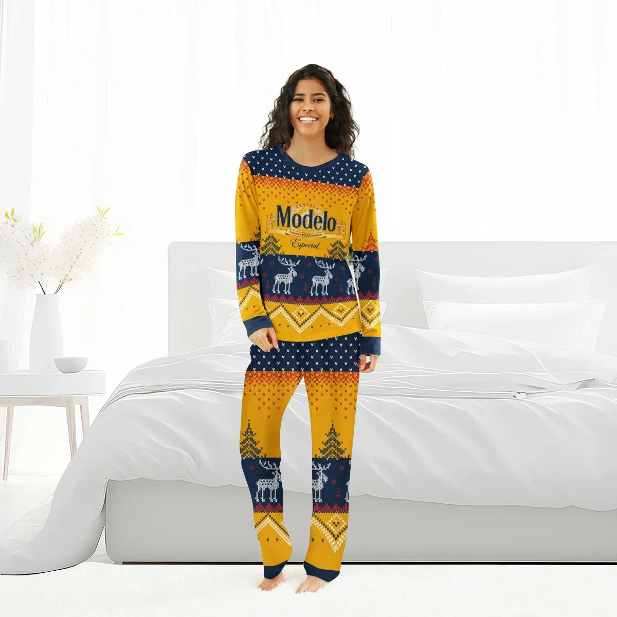 Smiling woman in Modelo-themed yellow and navy reindeer family pajamas standing barefoot in bright bedroom