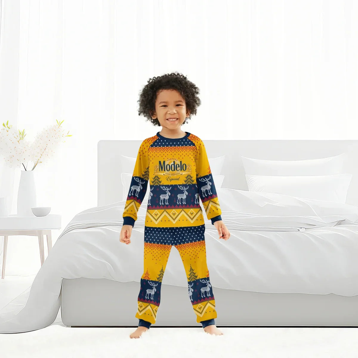 Smiling child wearing yellow and navy Modelo reindeer family pajamas standing in bright white bedroom